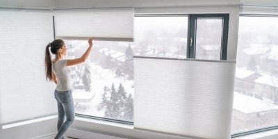 Mladá žena posouvá plisé rolety v moderním interiéru