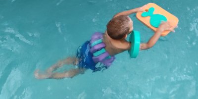 Dítě se učí plavat v bazénu s pěnovými pomůckami