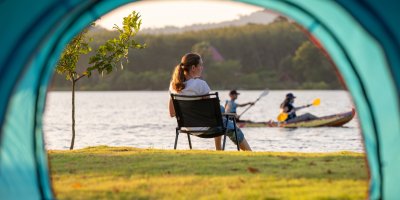 Žena sedí před stanem a dívá se na vodu