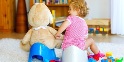 Malá holčička a její plyšový medvěd sedí na nočníku