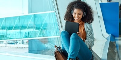 Žena sedící na letišti se sluchátky a tabletem