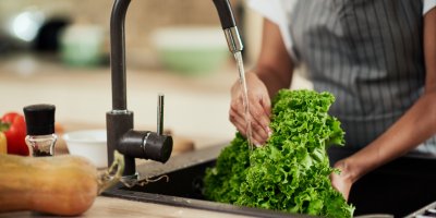 Člověk v zástěře omývá salát ve dřezu