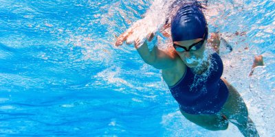 Žena plave pod vodou v jednodílných sportovních plavkách