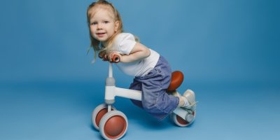 Holčička sedí na odrážedle v modrém studiu