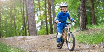 Chlapeček s přilbou a chrániči na loktech a kolenou jede na kole po lesní cestě