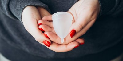 Menstruační kalíšek v rukou s nalakovanými nehty