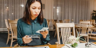 Žena v restauraci vytahuje bankovky z peněženky a přemýšlí
