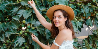 Žena v klobouku se natahuje pro fík rostoucí na fíkovníku na zahradě