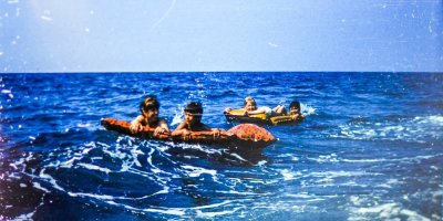 Stará fotografie ženy a dětí s nafukovacími lehátky v moři