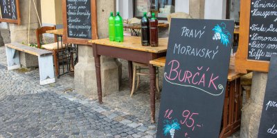 Cedule s nápisem „pravý moravský burčák“ před obchodem; vedle stůl s lahvemi burčáku