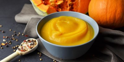 Dýňové pyré, lžíce s kořením a v pozadí dýně