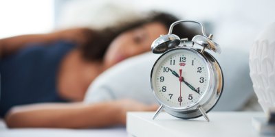 Budík, v pozadí žena spící na levém boku