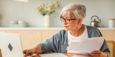 Seniorka s papíry v rukou u laptopu