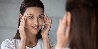 Žena se na sebe dívá v zrcadle a ruce má u očí