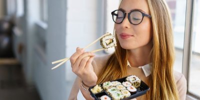 Mladá žena si pochutnává na sushi rolce z baleného sushi boxu