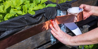 Člověk oblepuje vyvýšený záhon měděnou páskou 