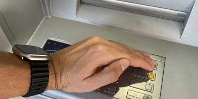 Člověk zakrývá rukou číselnou klávesnici bankomatu