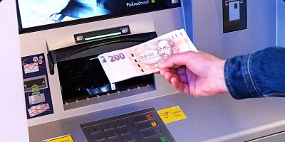 Člověk vkládá české bankovky do bankomatu