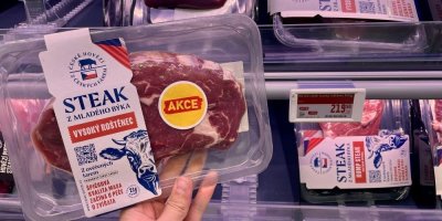 Ruka držící balený hovězí steak v supermarketu před regálem s masnými výrobky
