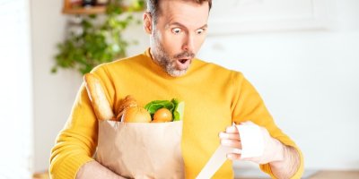 Muž drží nákup v papírové tašce a udiveně se dívá na účtenku