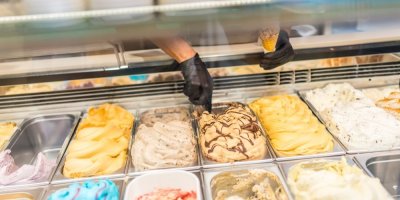 Člověk v černých rukavicích nabírá zmrzlinu do kornoutu