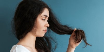 Žena si prohlíží konečky svých dlouhých tmavých vlasů.
