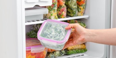 Žena vytahuje mražené fazolové lusky z mrazáku plného mražené zeleniny