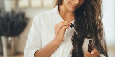 Žena si aplikuje přírodní olej do vlasů