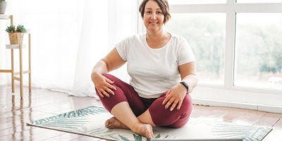 Žena středního věku sedí se skříženýma nohama doma na koberečku