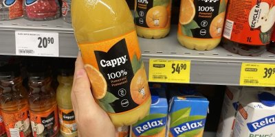 Mužská ruka držící pomerančový džus Cappy před regálem v supermarketu