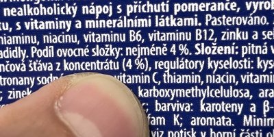 Detail prstu a etikety na obalu pomerančového džusu