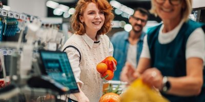 Mladá usmívající se zákaznice u pokladny supermarketu, prodavačka markující zboží