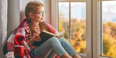 Dívka sedí za oknem a čte si