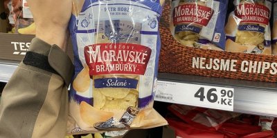 Mužská ruka drží balení brambůrků před regálem v supermarketu