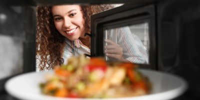 Žena dává talíř s jídlem do mikrovlnky