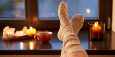 Nohy s dlouhými teplými ponožkami se opírají o okenní parapet se svíčkami