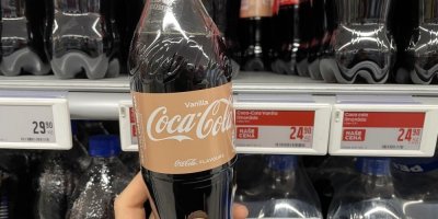 Ruka drží lahev Coca-Coly před regálem v supermarketu