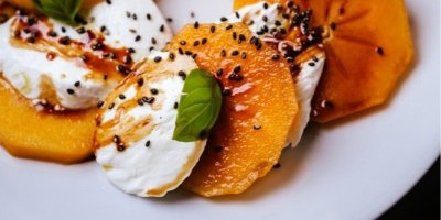 Plátky kaki a mozzarelly posypané černým sezamem a polité balsamicem