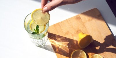 Ruka dává citronové plátky do sklenice s vodou