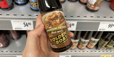 Ruka držící sójovou omáčku před regálem v supermarketu