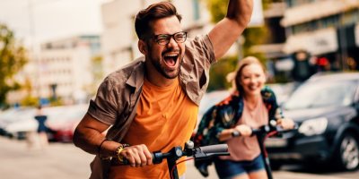 Mladý veselý pár jede na koloběžkách po městě