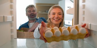 Žena dává vejci do lednice, za ní je vysmátý muž
