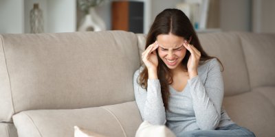 Žena sedí na gauči a bolí ji hlava