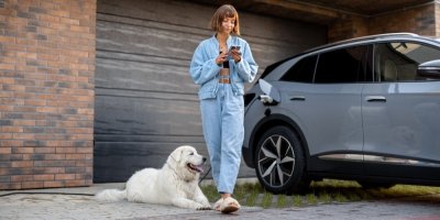 Žena se psem stojí u nabíjejícího se elektromobilu