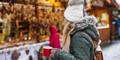 Žena s hrnkem v ruce stojí na náměstí na vánočním trhu
