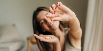 Mladá usmívající se žena drží v ruce potravinové doplňky a jeden z nich ukazuje na kameru