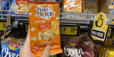 Ruka držící balení sýrového popcornu před regálem v supermarketu