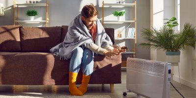 Muž je zabalený v dece a ohřívá si ruce o přímotop