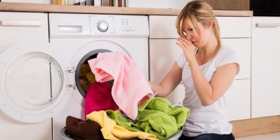 Žena vyndává prádlo z pračky a drží si nos