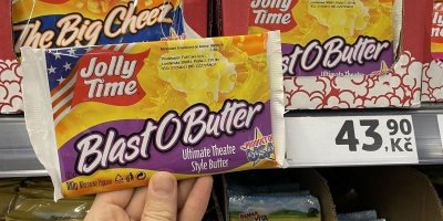 Ruka držící balení popcornu před regálem supermarketu